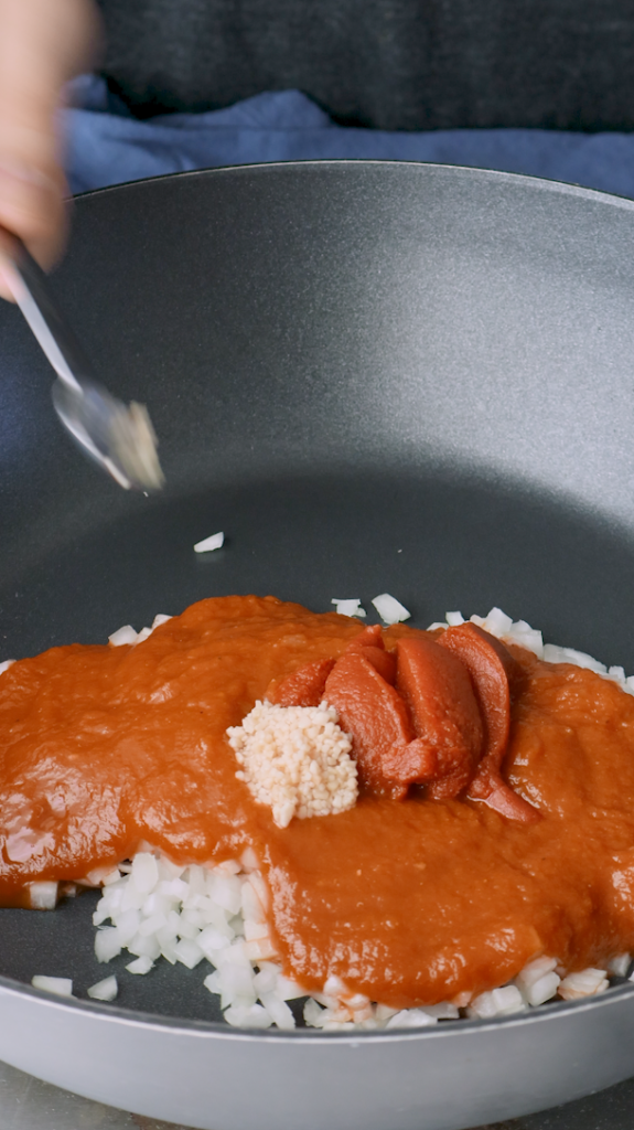 Next add diced onion, tomato sauce, tomato paste, minced garlic, turmeric, and coriander to a large pan. 